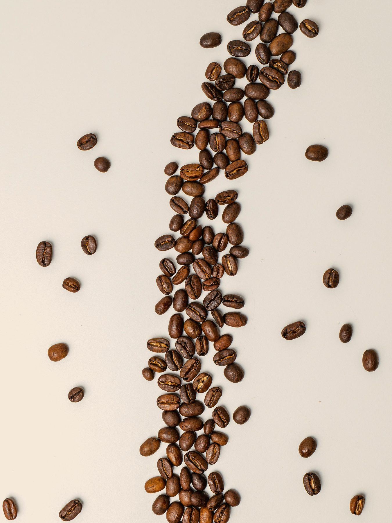 Roasted coffee beans scattered in a loose line across a pale surface