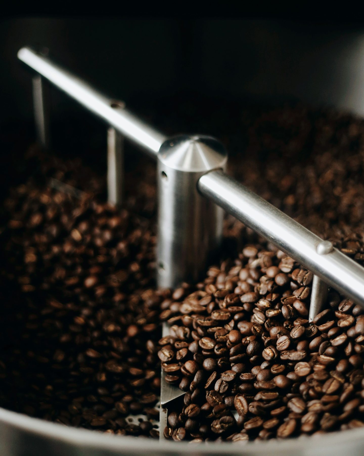 Freshly roasted coffee beans turned by the steel arm of a roaster’s cooling tray