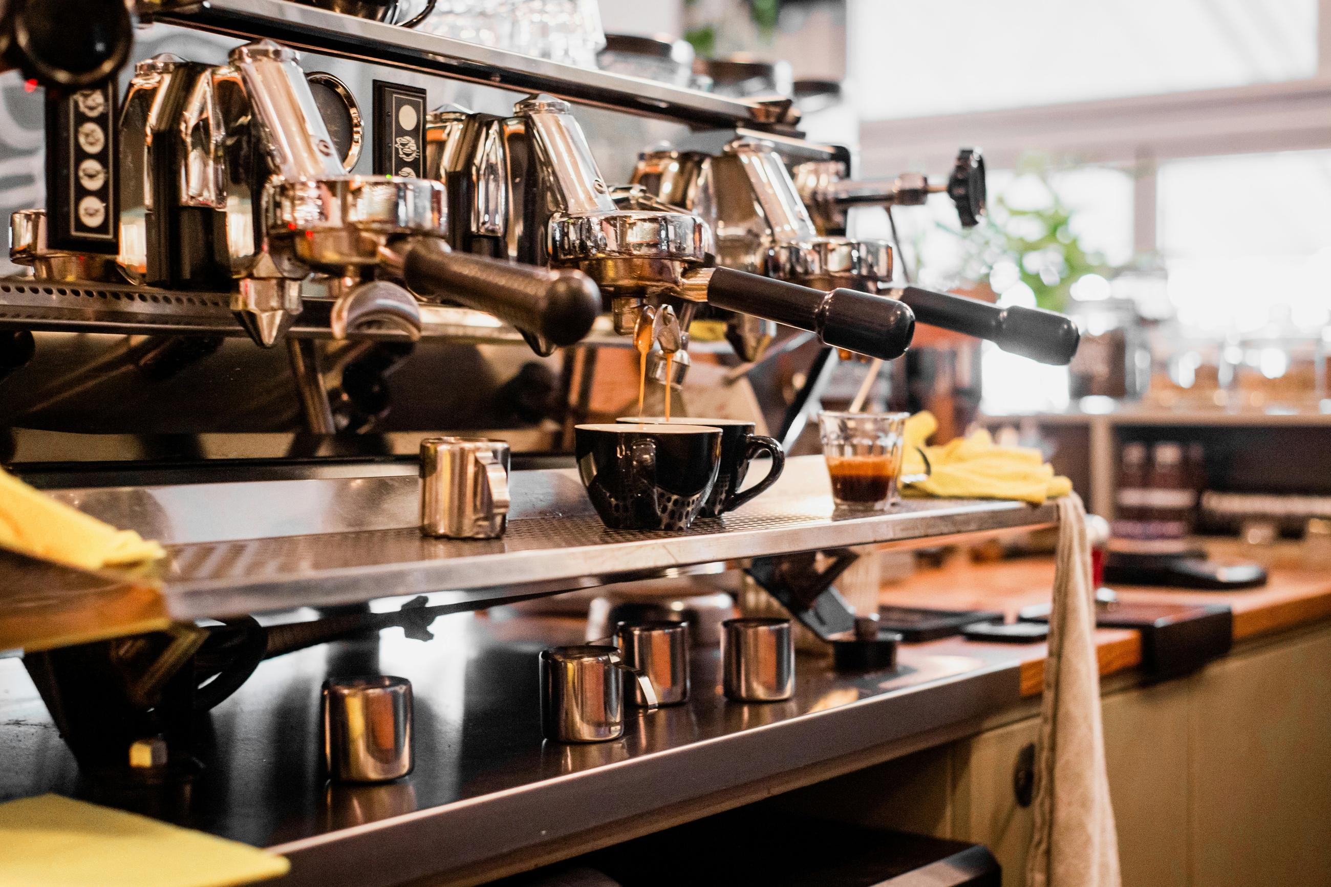 A multi-group espresso machine pulling two shots into black cups on a bright café bar