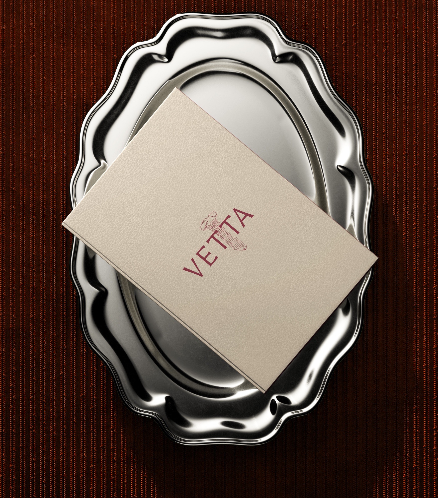 A cream VETTA menu card resting on a scalloped silver tray over dark red ribbed fabric